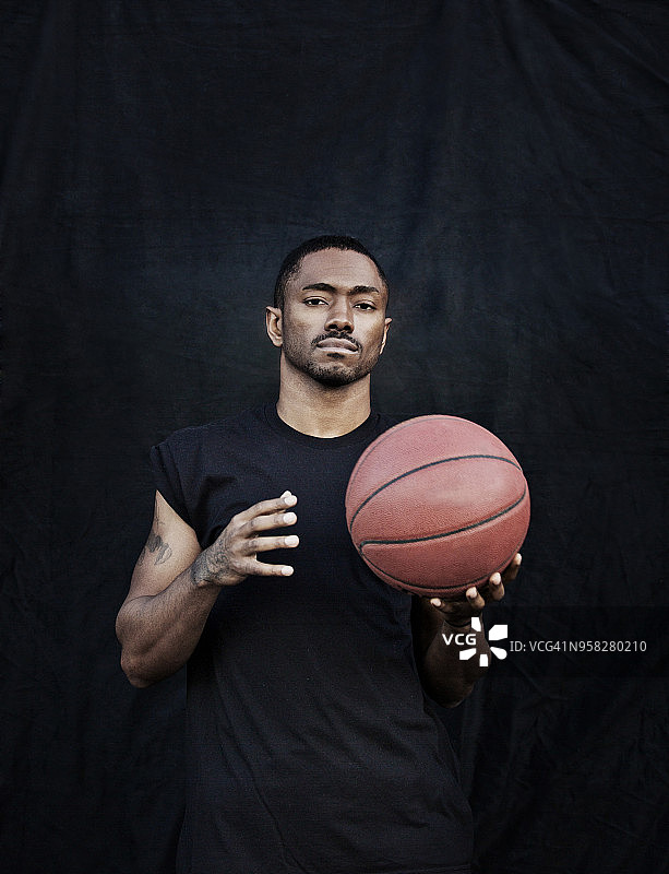 一个男人拿着篮球，背靠黑色的墙站着图片素材