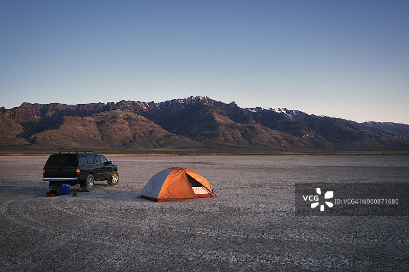 帐篷和汽车在干燥的土地上，背靠高山和天空，在阿尔沃德沙漠图片素材