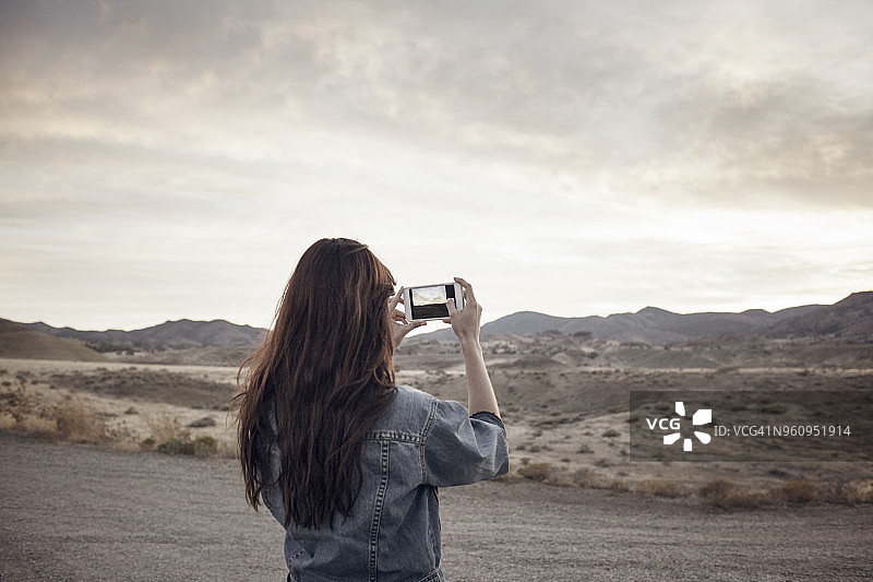 女子站在野外拍摄山景的后视图图片素材