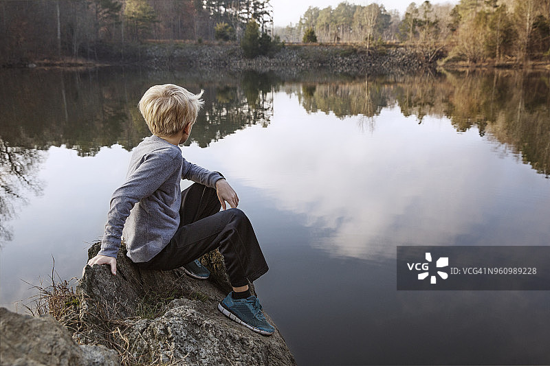 男孩坐在湖边的岩石上图片素材