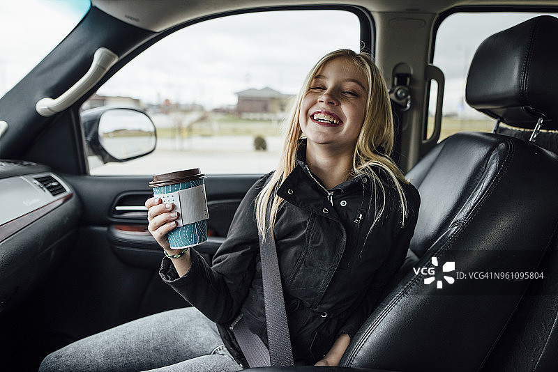 坐在车里拿着一次性杯子的快乐女孩图片素材