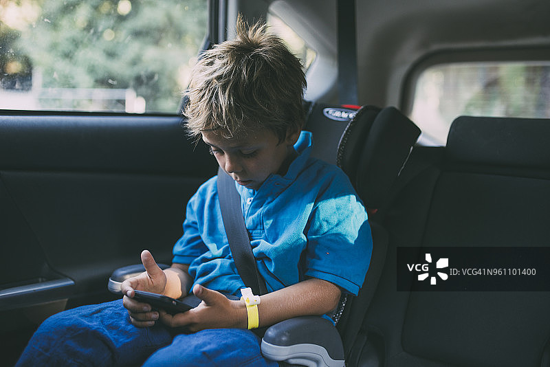 坐在车里玩智能手机的男孩图片素材