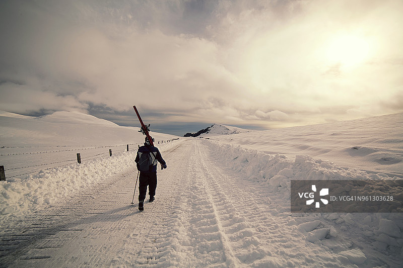 在多云的天空下，在雪景上行走的人的后视图图片素材