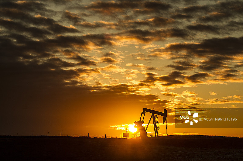 中距离剪影抽油机在石油工业对多云的天空在日落图片素材