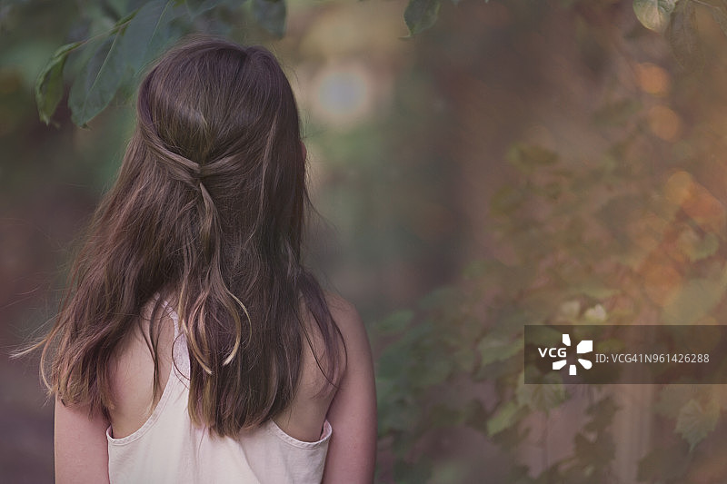 一个棕色长发穿着粉色背心的年轻女孩站在树林的边缘图片素材