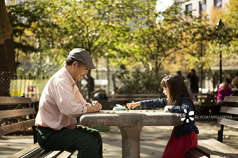 爷爷和孙女坐在公园的桌子旁玩棋盘游戏图片素材
