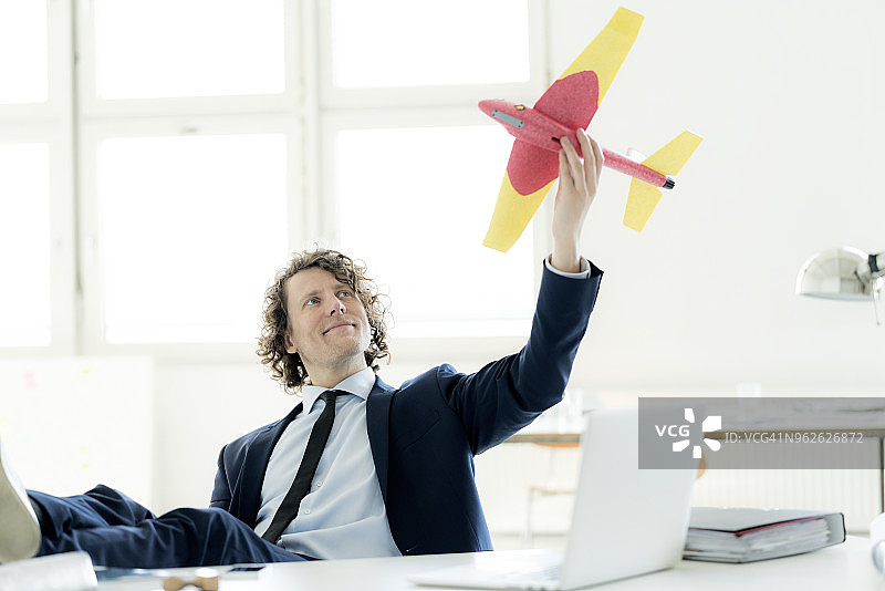 一个商人坐在他的办公室里玩玩具飞机图片素材