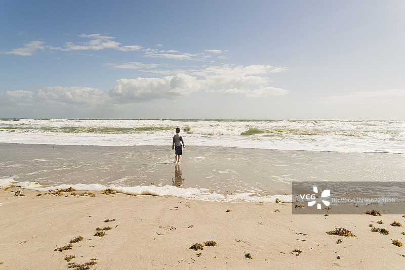 在阳光明媚的日子里，男孩站在海滩上的背影图片素材