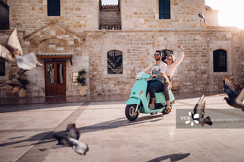 年轻夫妇有乐趣骑老式摩托车在欧洲小镇图片素材