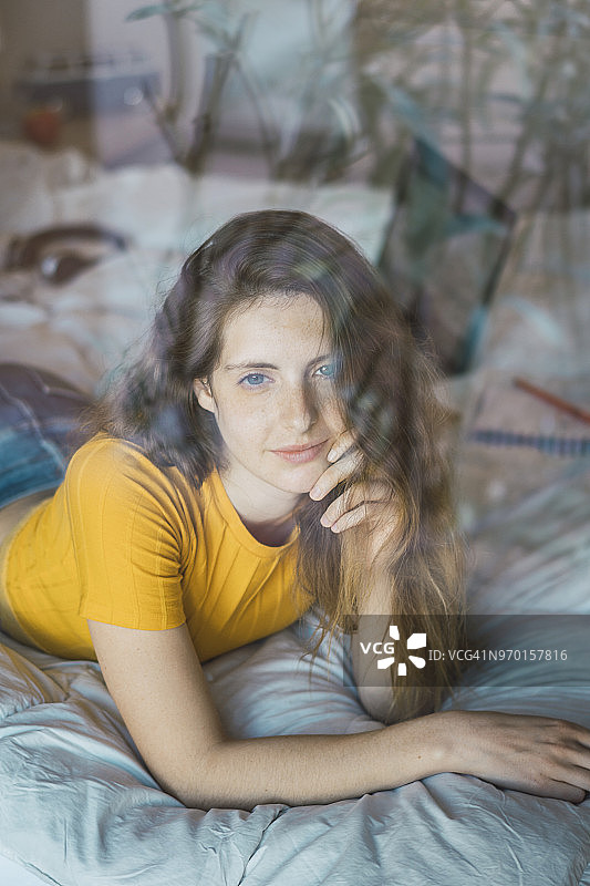 一幅微笑的年轻女子的肖像，躺在窗户后面的床上图片素材