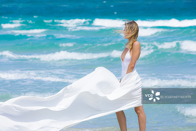 年轻女子在一个田园诗般的海滩上拿着白色的织物图片素材