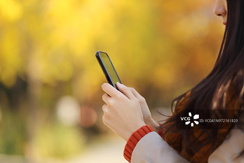 一名年轻女子在秋季公园使用智能手机图片素材