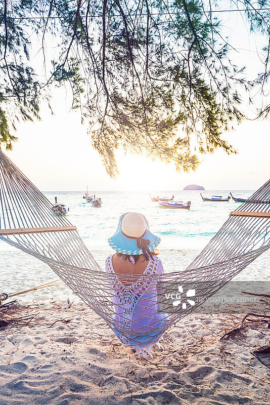 日落时分，一个女人坐在热带海滩的吊床上图片素材