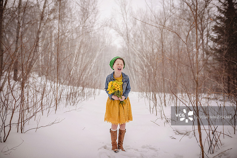 微笑的女孩站在雪中，拿着一束黄花图片素材
