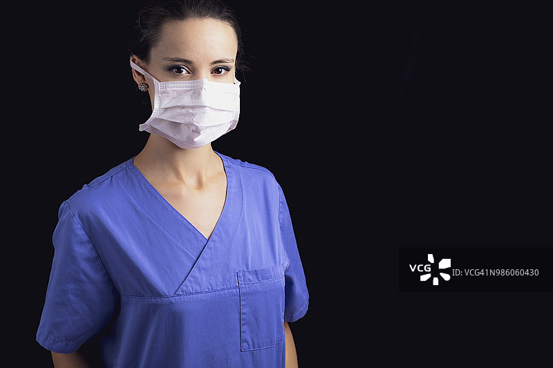 年轻女医生的肖像，穿着蓝色的手术服和口罩，在黑色的背景。图片素材