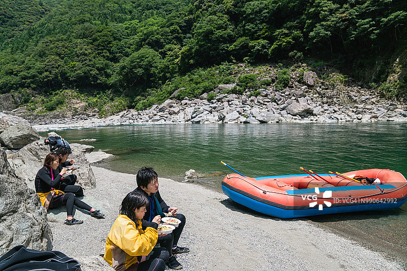 一小群男人和女人在海滩上吃午餐，同时在河边泛舟图片素材