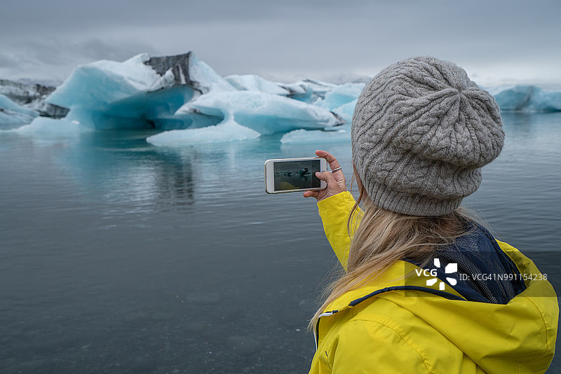 年轻女子用手机拍摄冰川湖，冰山漂浮在水面上图片素材