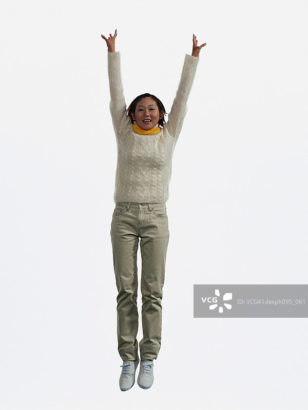 年轻的亚洲女人在裤子和运动衫和围巾，跳在半空中图片素材