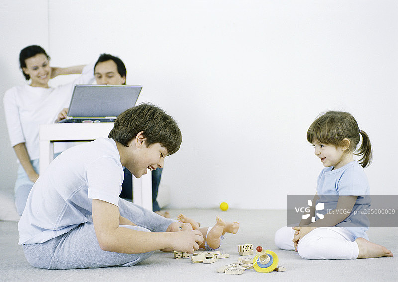 男孩和女孩坐在地板上玩，男人和女人在后台使用笔记本电脑图片素材