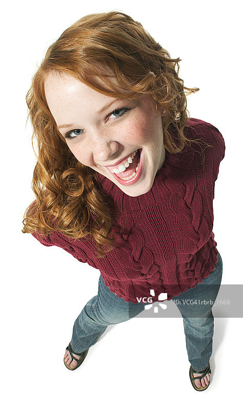 一个穿着牛仔裤和红色毛衣的白人红发少女对着镜头笑个不停图片素材