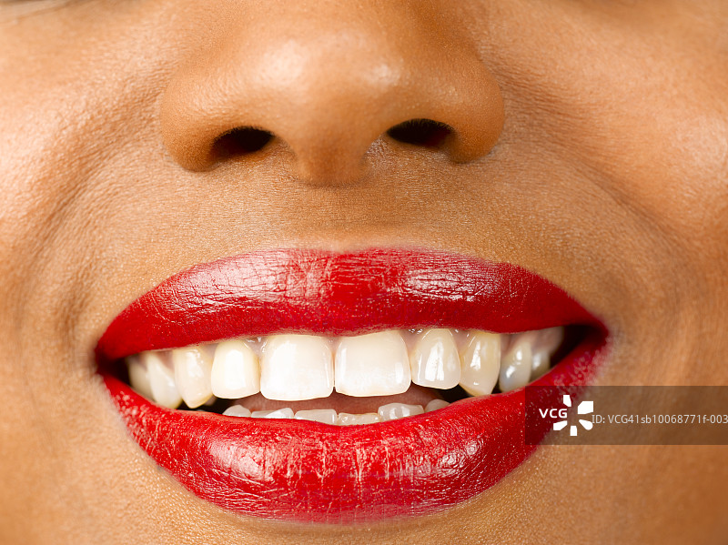 女人抹着红色的口红微笑着，近距离的嘴，摄影棚拍摄图片素材