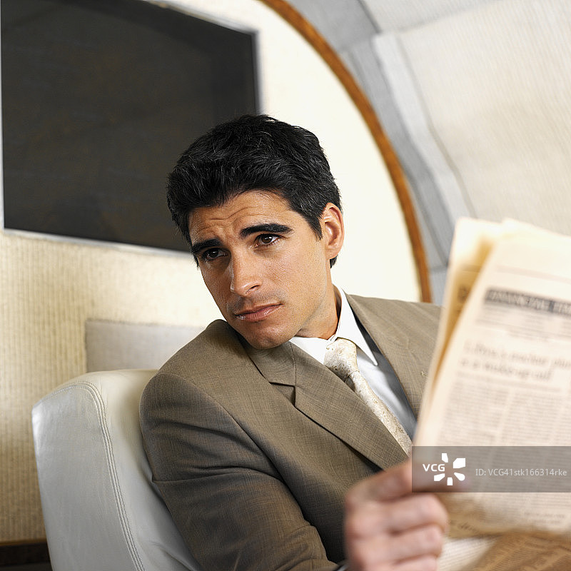 近距离的商人分心，而阅读报纸在头等舱飞机图片素材