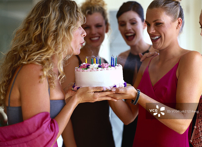 一个女人和朋友吹灭生日蛋糕上的蜡烛的侧影图片素材