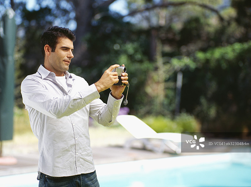 在泳池边用家庭摄像机拍摄的中年男子图片素材