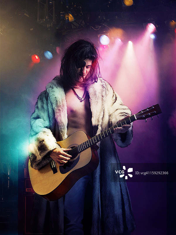 穿着裘皮大衣的年轻摇滚音乐家在音乐会上弹吉他图片素材