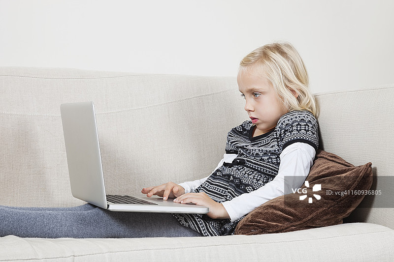年轻女孩在沙发上使用笔记本电脑的侧视图图片素材
