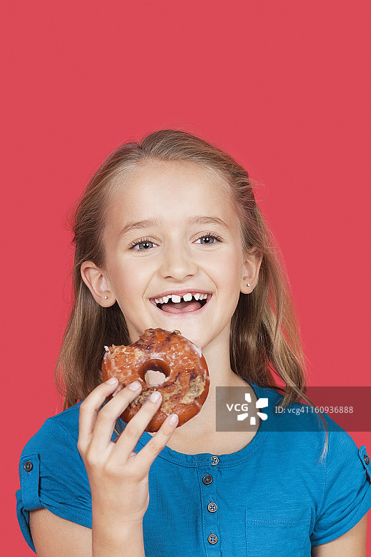 肖像快乐的年轻女孩拿着甜甜圈在红色的背景图片素材