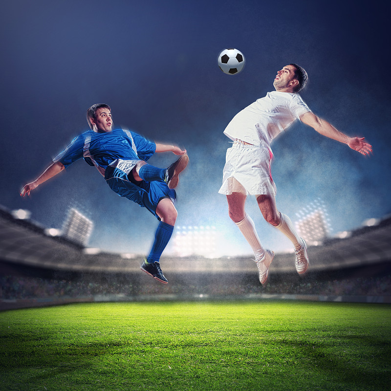 两个足球运动员击球。两名足球运动员在体育场上跳起击球图片下载