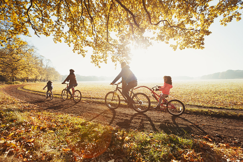 年轻的家庭骑在阳光明媚的秋天公园图片素材