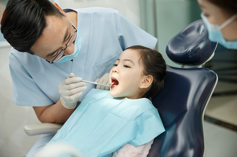 男牙医和女牙医助手在为小女孩检查牙齿图片下载