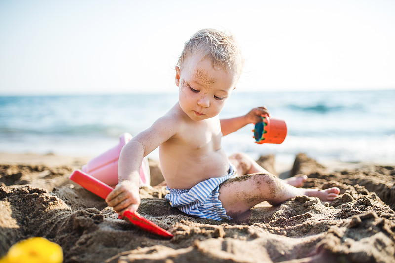 暑假，一个蹒跚学步的小女孩坐在海滩上玩耍。图片下载