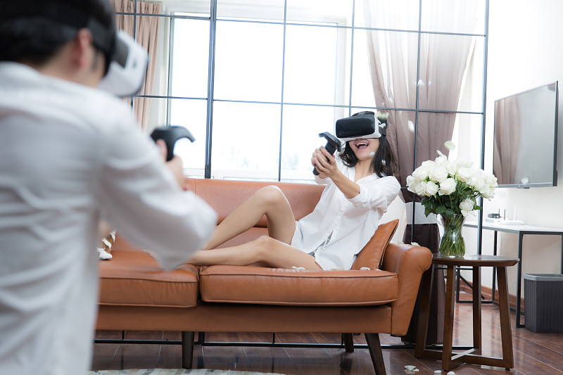 青年情侣在客厅戴着VR眼镜拿着游戏手柄一起玩游戏图片下载
