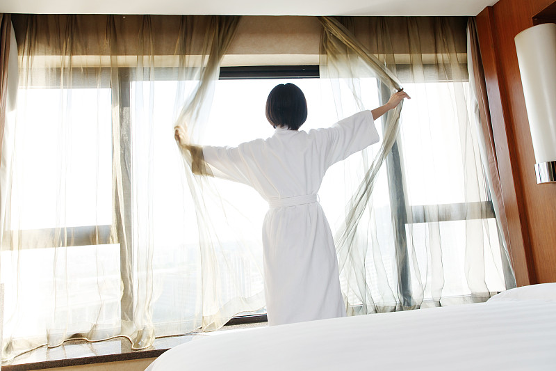 年轻女人在酒店房间里拉开窗帘图片素材