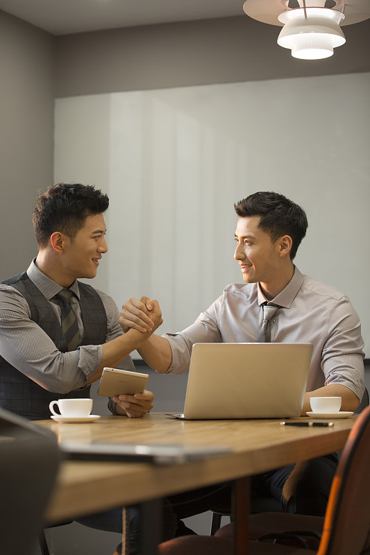 商务青年男子使用笔记本电脑在公司会议室讨论工作握手庆祝达成共识图片素材