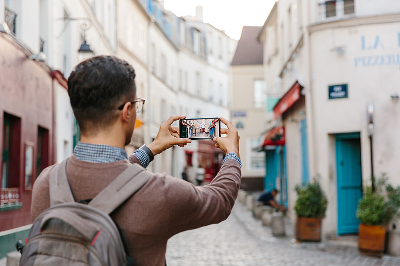 一个年轻人用智能手机拍摄蒙马特大街的后视图，巴黎，法国图片素材
