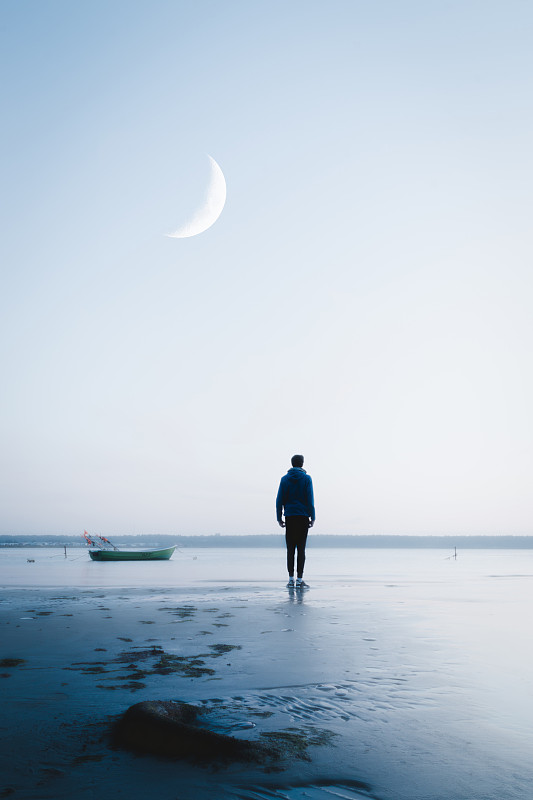在日落时，十几岁的男孩站在海滩上图片素材