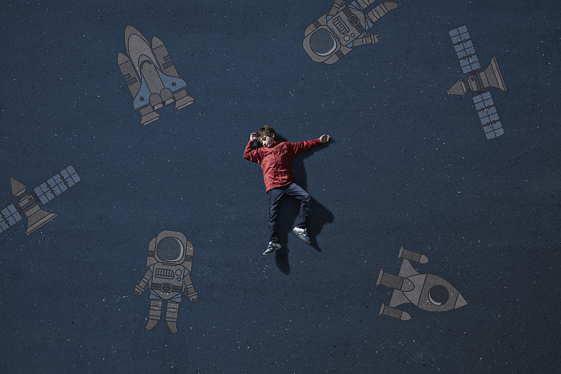 男孩躺在太空旅行的物体中间，画着想象的背景图片素材
