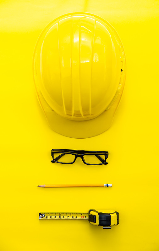 在黄色的背景上用眼镜和卷尺测量的铅笔的Hardhat的直接上面的观点图片下载