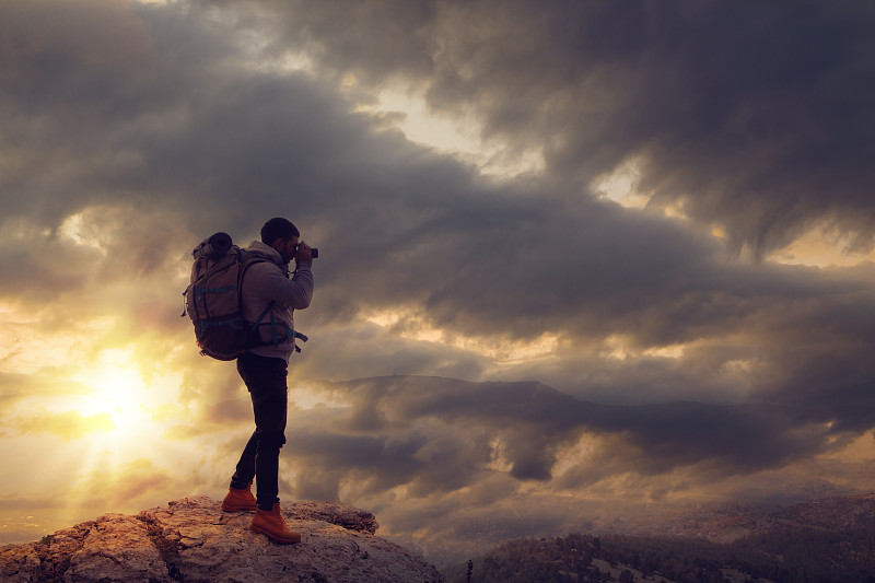 年轻的旅行者在山上拍摄夕阳下的照片。摄影图片
