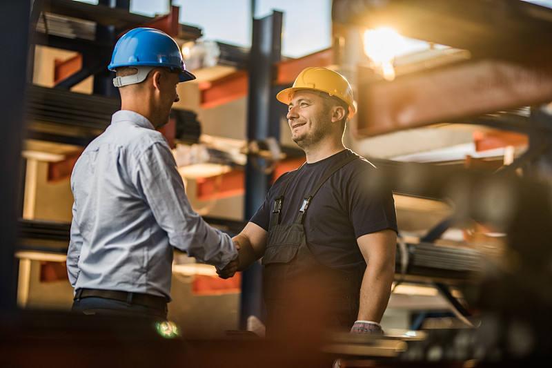 快乐的金属工人在仓库里与经理握手。图片下载