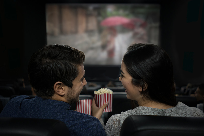 一对幸福的情侣在看电影吃爆米花，玩得很开心图片素材