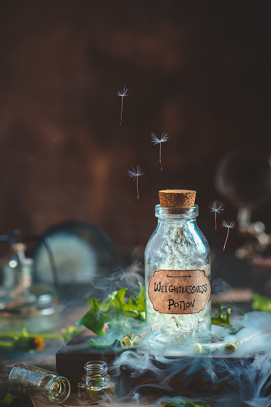 玻璃药水瓶蒲公英种子和手工制作的标签在一个神奇的静物与烟图片下载
