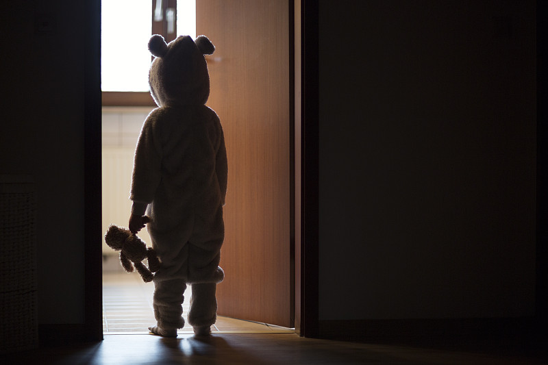 孩子穿着熊的服装，站在黑暗的门口，望着灯光图片素材