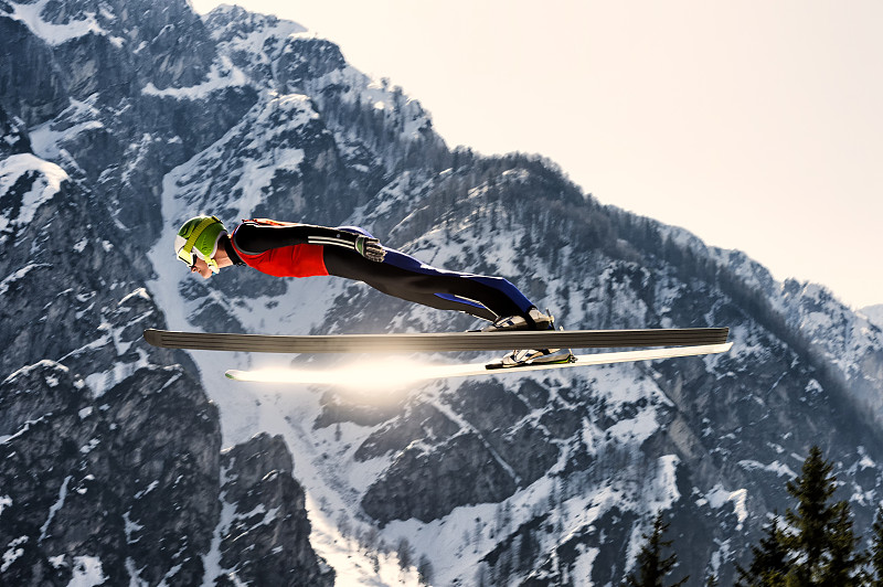 侧视图的年轻男子滑雪跳台在半空中，太阳反射图片下载
