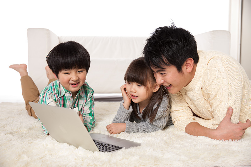 父亲和儿女趴在地毯上使用掌上电脑图片素材