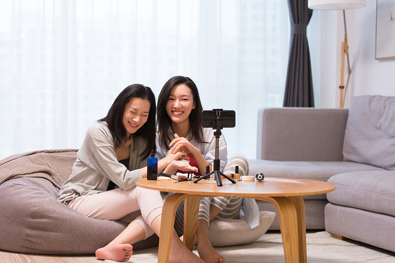 两个年轻女闺密在起居室化妆美容护肤做网络直播图片素材